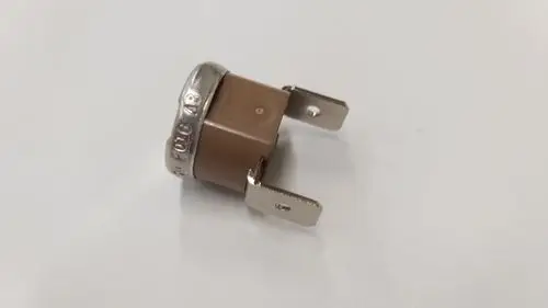 Brauner Temperaturbegrenzer mit metallischem Rand und zwei Anschlüssen, im Hintergrund weiß. Produkt von Remeha.